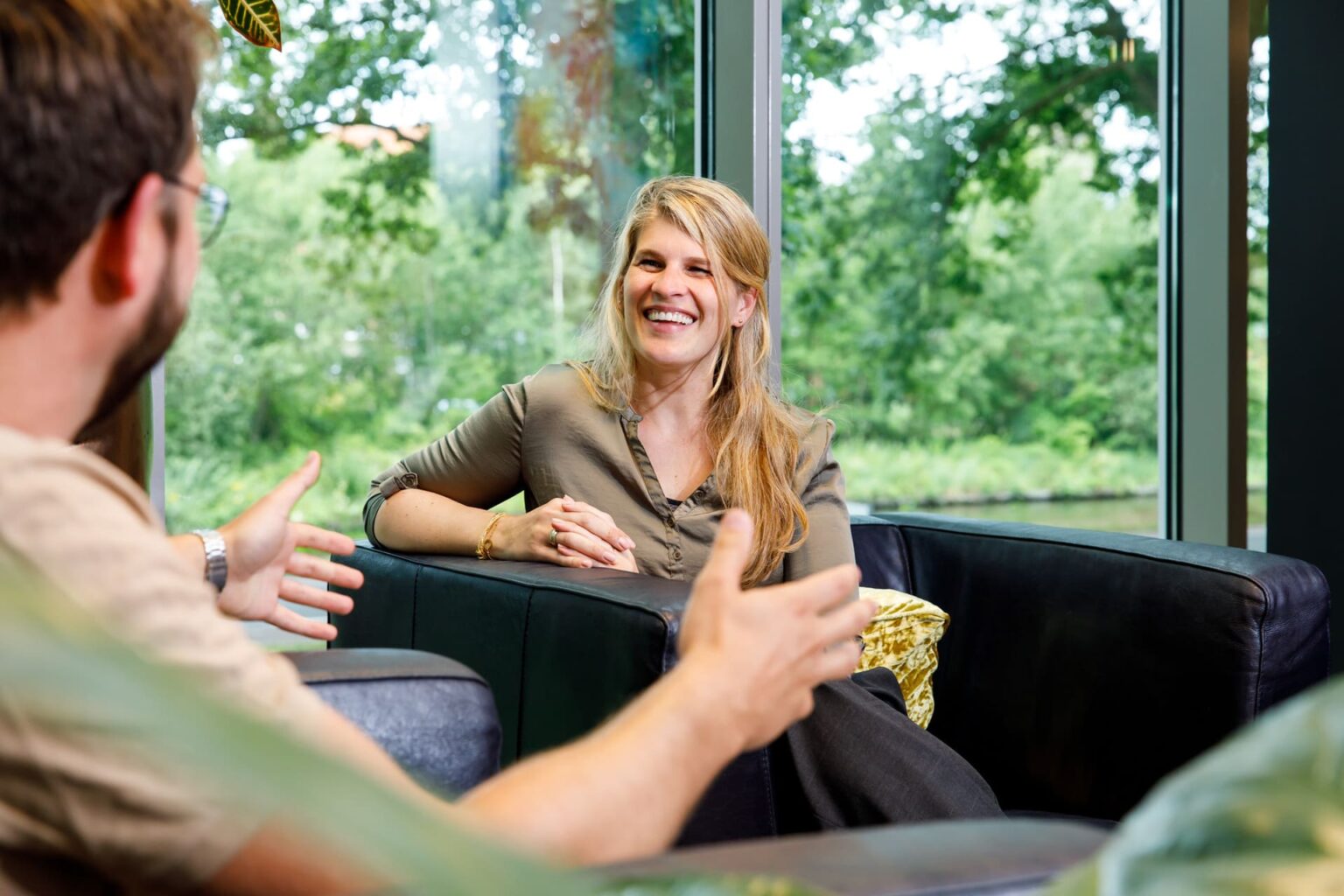 Man en vrouw in gesprek over persoonlijke coaching bij coaching2do in een zwarte leren stoel bij een groot raam met veel groen