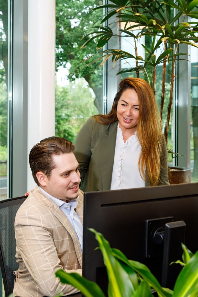 Collega's samenwerken aan een computerscherm in een groene kantooromgeving