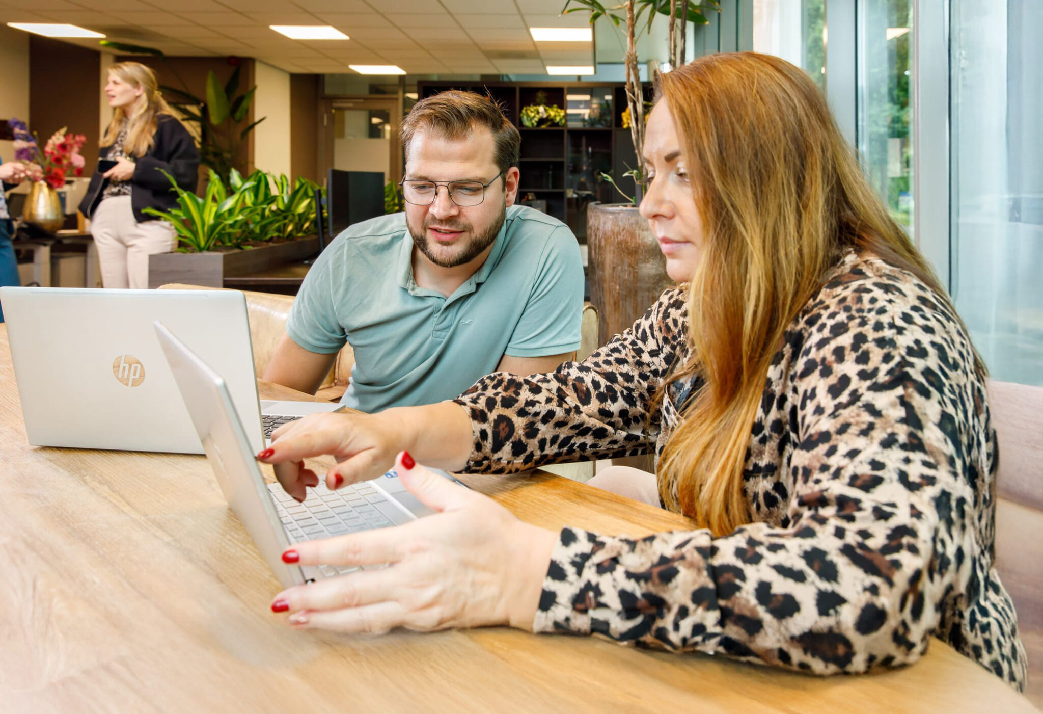 Collega's aan het werk met laptops in een moderne kantooromgeving, gefocust op samenwerking.