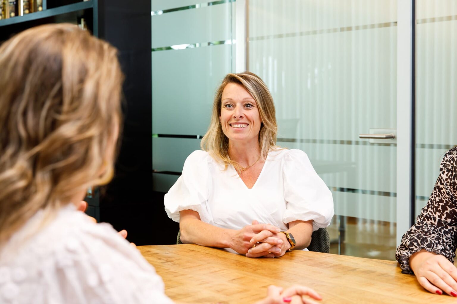 Vrouw in witte blouse glimlacht tijdens een zakelijk overleg in een modern kantoor van coaching2do